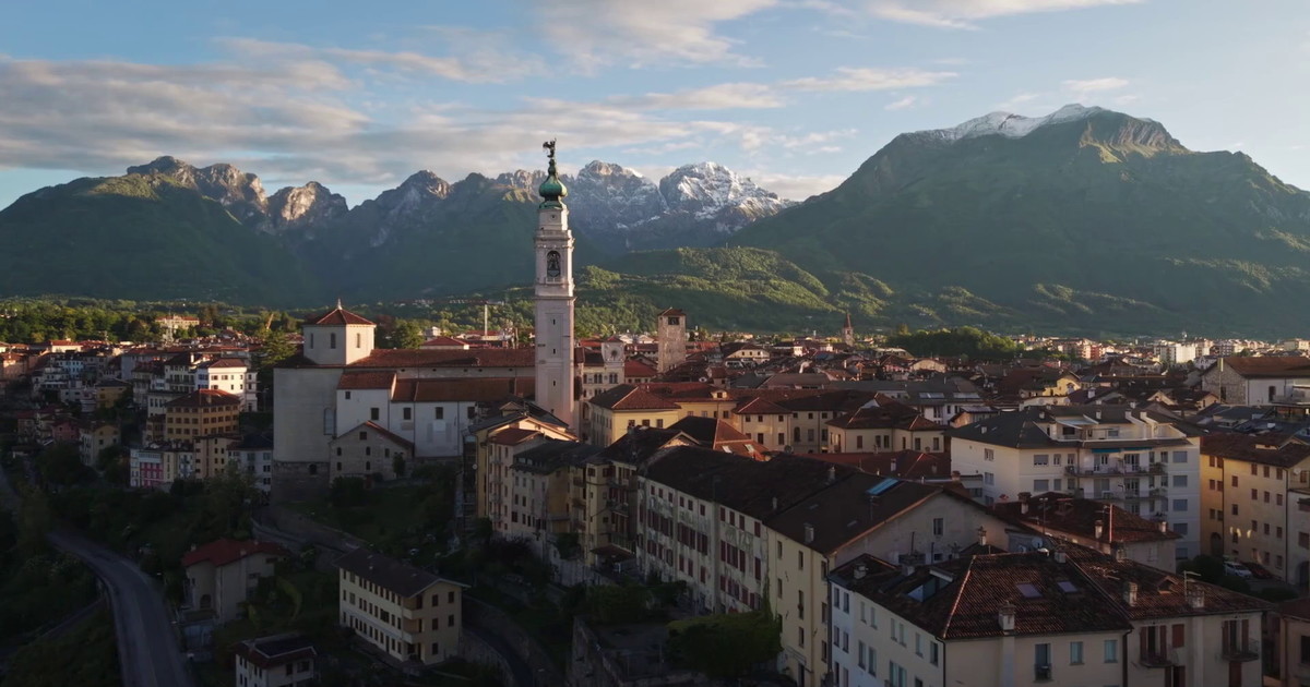Paesaggio montano con borgo storico, visitatori che passeggiano tra vicoli, edifici tradizionali circondati dalla natura, immagine di approfondimento